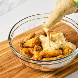 Bowl of fried wings being drizzled with creamy sauce on a wooden surface
