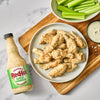 A bottle of Frank's RedHot Buffalo Ranch sauce is displayed next to a plate of chicken wings coated in the same sauce, accompanied by celery sticks and a bowl of ranch dressing.