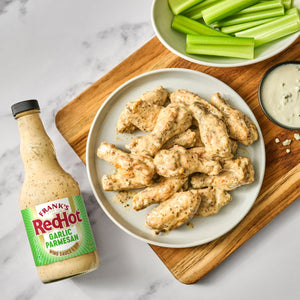 A bottle of Frank's RedHot Buffalo Ranch sauce is displayed next to a plate of chicken wings coated in the same sauce, accompanied by celery sticks and a bowl of ranch dressing.