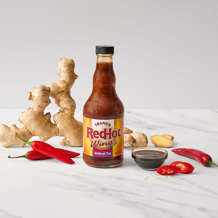 A bottle of Franks RedHot Wings General Tso sauce is displayed with ginger and red chili peppers.