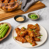 A plate of glazed chicken wings sprinkled with sesame seeds and green onions is displayed with celery sticks sesame seeds and green onions in bowls.
