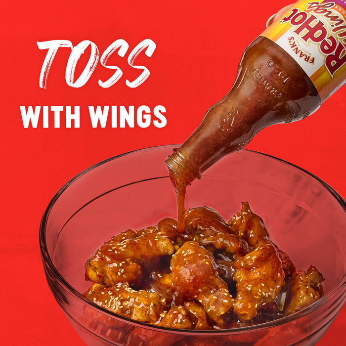 A bottle of Franks RedHot Wings sauce is being poured over a bowl of chicken wings.