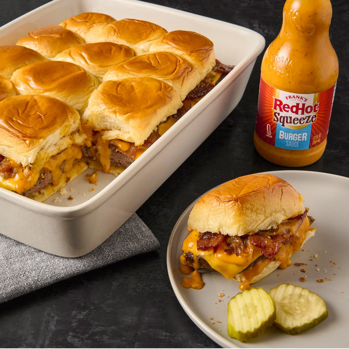 A plate of Franks RedHot Squeeze Burger Sauce with a cheeseburger slider and pickles.