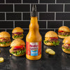 A bottle of Franks RedHot Squeeze Burger Sauce sits in front of six mini cheeseburgers.
