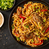 A plate of noodles with beef peppers and green onions.