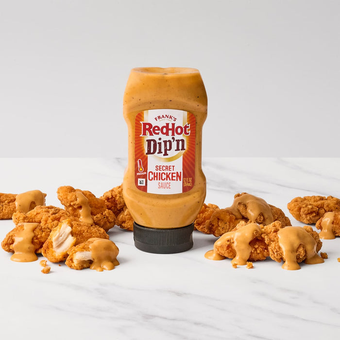 A bottle of Franks RedHot Dipn Secret Chicken Sauce is surrounded by fried chicken tenders drizzled with the same sauce.
