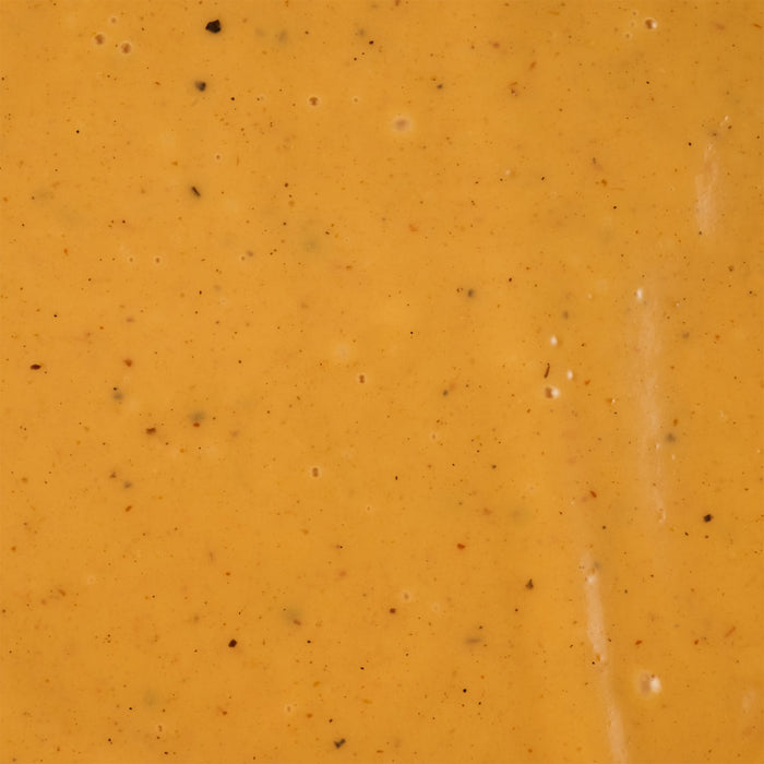 A close-up shot of a smooth orange-colored sauce with small specks of herbs and spices.