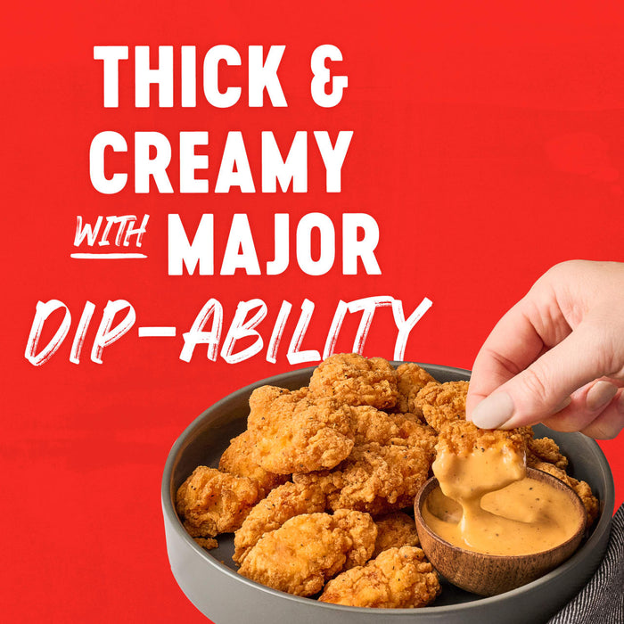 A hand dips a crispy chicken nugget into a bowl of thick creamy sauce highlighting its major dip-ability.