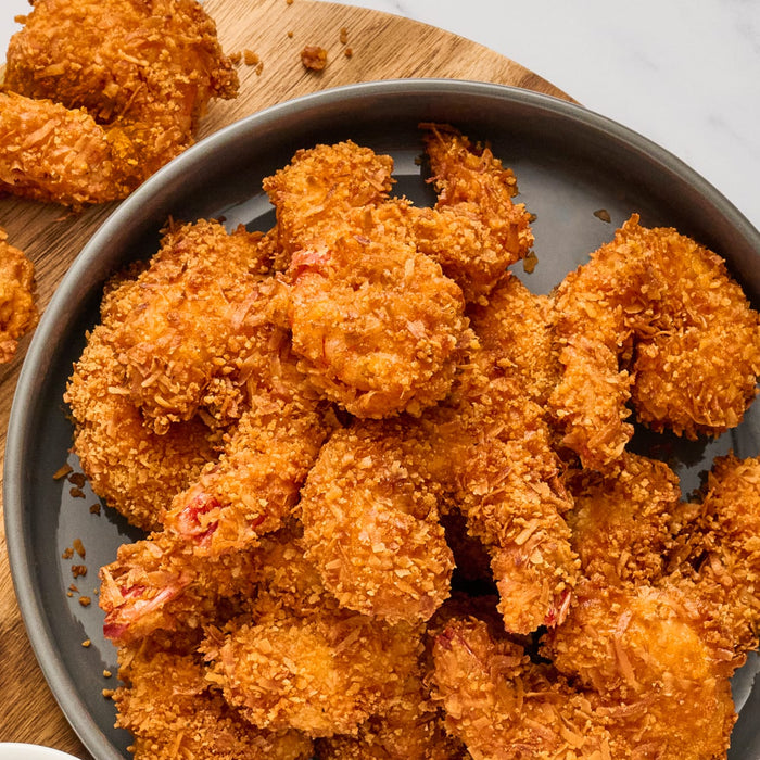 A plate of golden-brown crispy coconut shrimp is presented on a wooden board showcasing a delicious seafood dish.