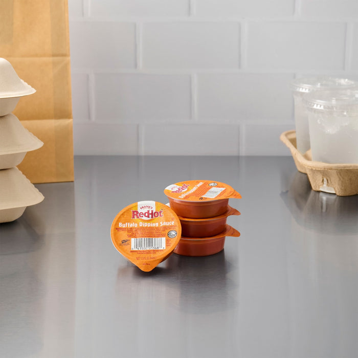 A stack of individual Hellman's mayonnaise condiment cups sits on a stainless steel surface.