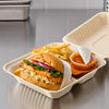 A takeout container displays a burger with fries and a side of sauce, showcasing a convenient meal option.