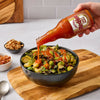A bowl of food is being drizzled with a bottle of Padillo hot sauce.