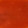 A close-up shot of vibrant red tomato soup with visible specks of herbs and spices.