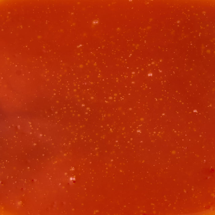 A close-up shot of vibrant red tomato soup with visible specks of herbs and spices.