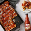A pan of French toast casserole drizzled with Frank's RedHot sauce is shown with a serving on a plate and a bottle of the sauce.