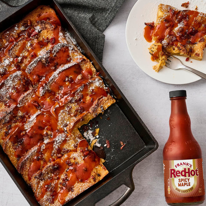 A pan of French toast casserole drizzled with Frank's RedHot sauce is shown with a serving on a plate and a bottle of the sauce.