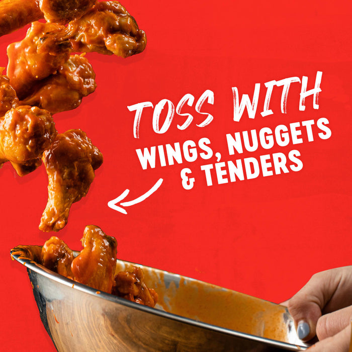 Wings, nuggets, and tenders are being tossed in a bowl with sauce.
