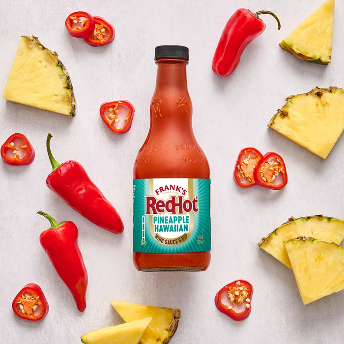 A bottle of Frank's RedHot Sweet Chili sauce is surrounded by red chili peppers and splatters of yellow sauce.