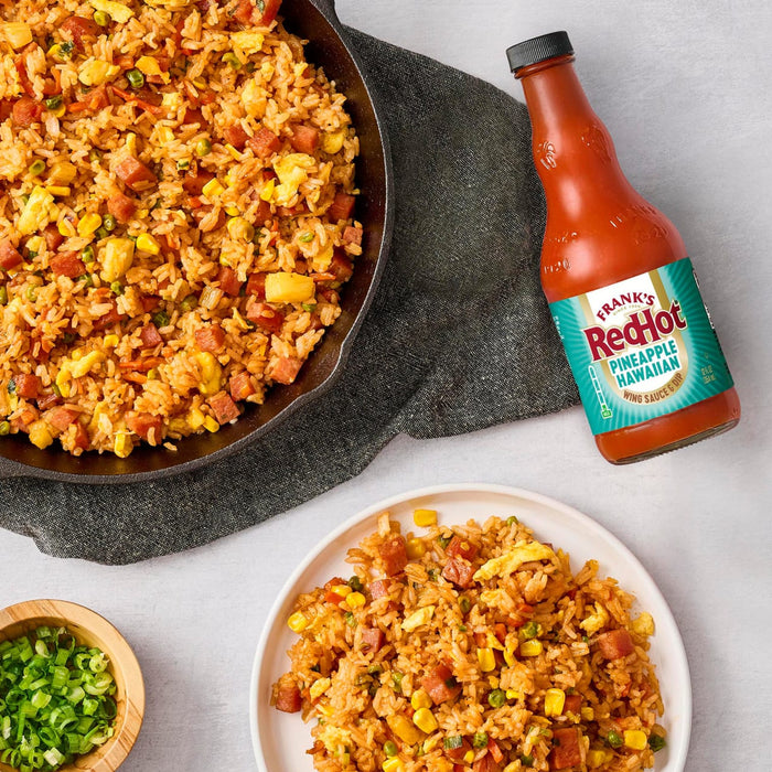 A plate and skillet of fried rice with a bottle of Frank's RedHot sauce next to it.