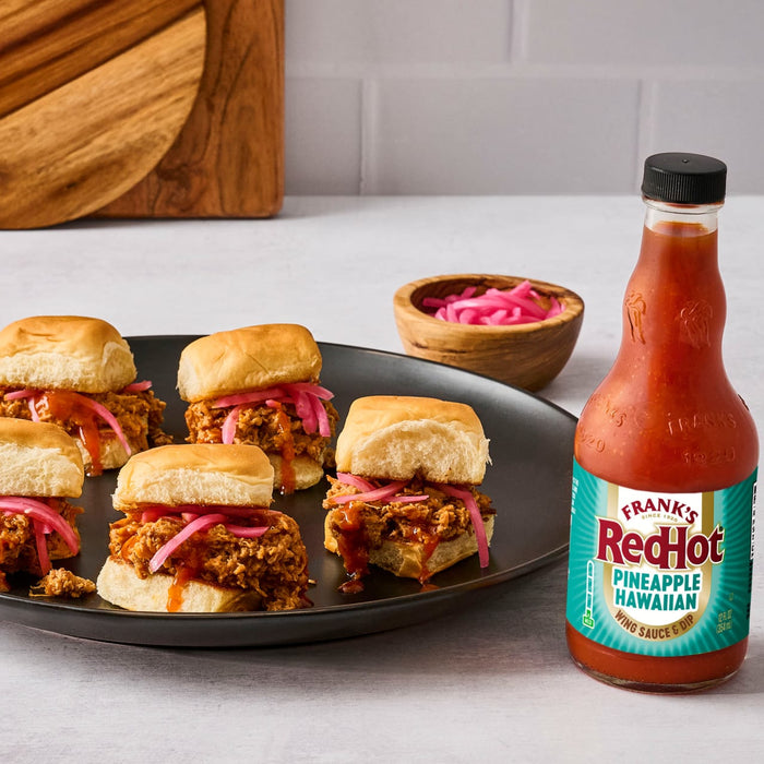A plate of mini sandwiches topped with pink onions is displayed next to a bottle of Frank's RedHot Pineapple Habanero Sauce.