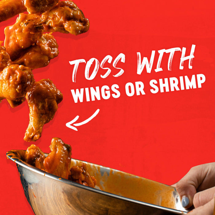 A close-up of chicken wings being tossed in a metal bowl with a sauce, suggesting the product can be used to toss with wings or shrimp.