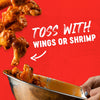 A close-up of chicken wings being tossed in a metal bowl with a sauce, suggesting the product can be used to toss with wings or shrimp.
