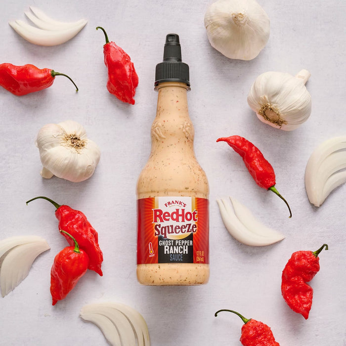 A bottle of Frank's RedHot Creamy Garlic Sauce is surrounded by garlic bulbs, cloves, and red chili peppers.