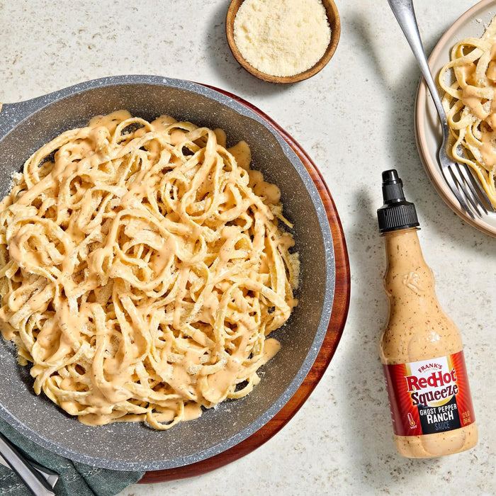 A pan of fettuccine Alfredo with a bottle of Arfons Alfredo Sauce and a bowl of parmesan cheese.