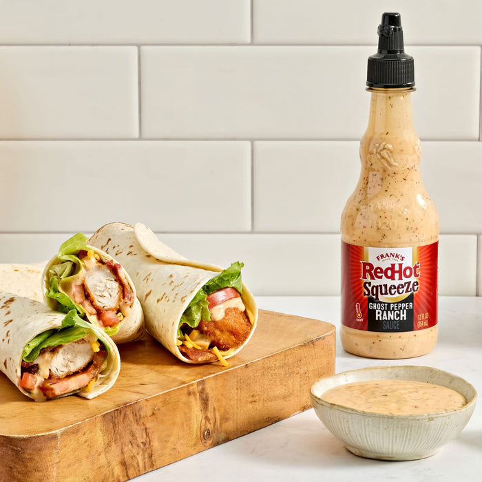 Three chicken wraps are displayed on a wooden board next to a bottle of Red Gold Ketchup Secret Sauce and a small bowl of the same sauce.