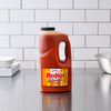 A large bottle of Frank's RedHot Wings Spicy Maple Sauce sits on a stainless steel countertop.
