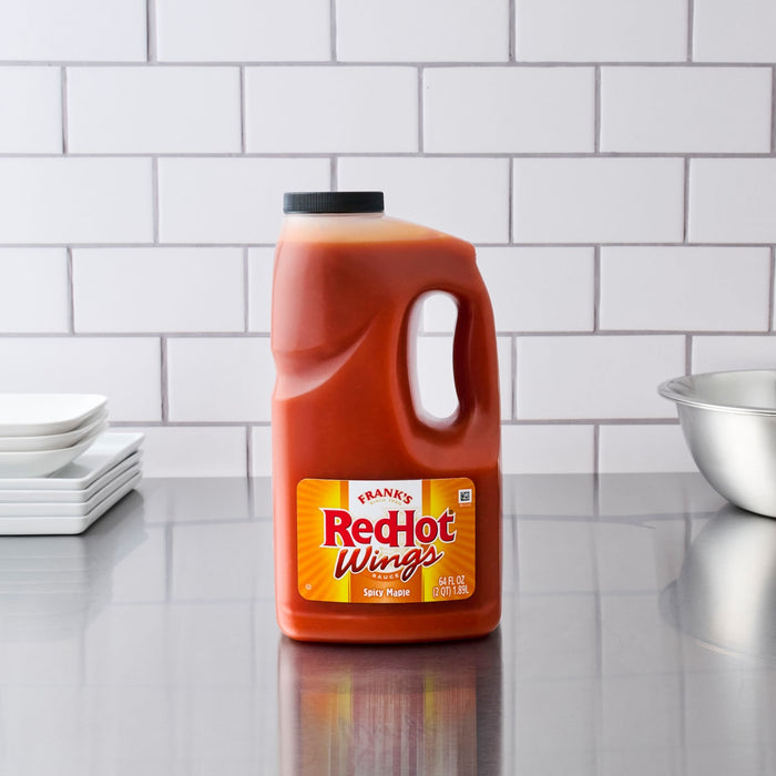 A large bottle of Frank's RedHot Wings Spicy Maple Sauce sits on a stainless steel countertop.