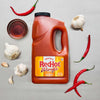 A bottle of Frank's RedHot Wings Spicy Maple sauce is surrounded by garlic cloves, red chili peppers, and a bowl of liquid.