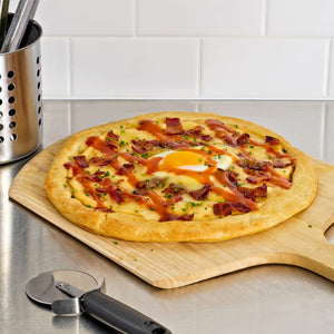 A breakfast pizza topped with bacon, cheese, chives, and a fried egg is presented on a wooden cutting board with a pizza cutter nearby.