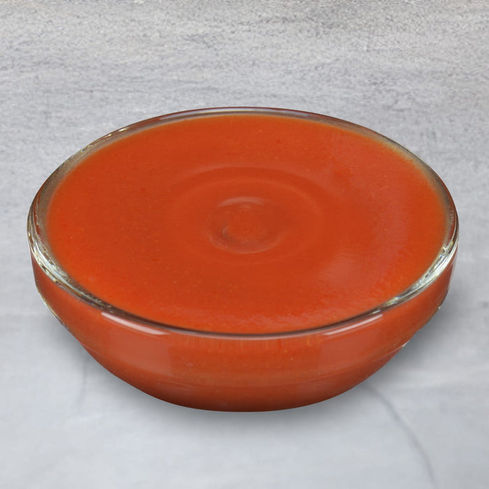 A bowl of tomato soup sits on a marble surface.