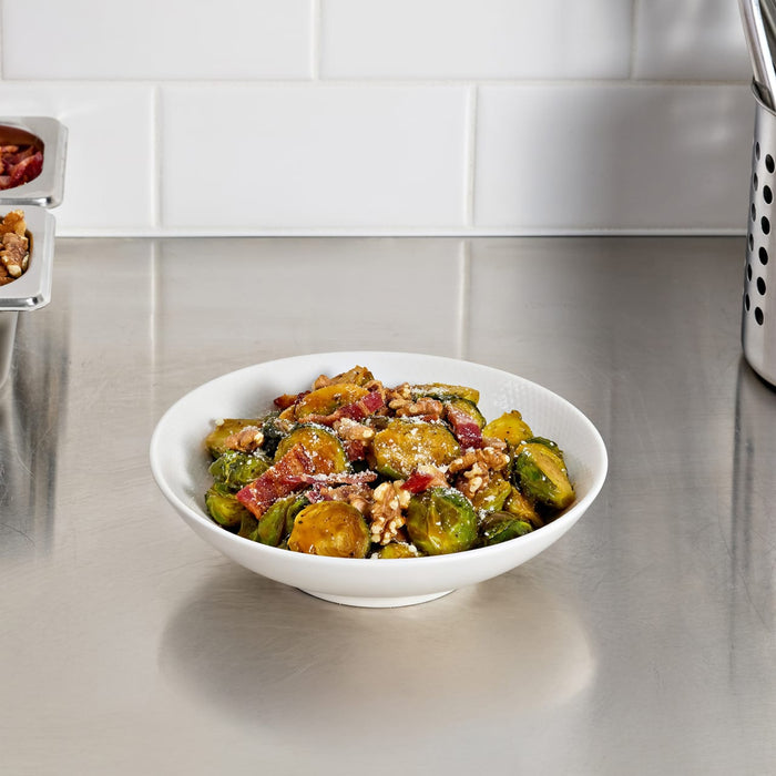 A bowl of Brussels sprouts with bacon and walnuts sits on a stainless steel countertop.