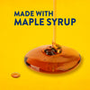 Maple syrup is drizzled onto a yellow surface, highlighting the product's key ingredient.