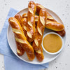 A plate of pretzel sticks with a side of mustard for dipping.