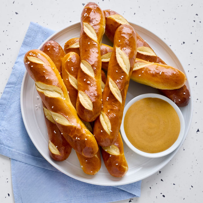 A plate of pretzel sticks with a side of mustard for dipping.