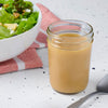 A jar of homemade salad dressing sits next to a fresh salad, suggesting a healthy and delicious meal option.