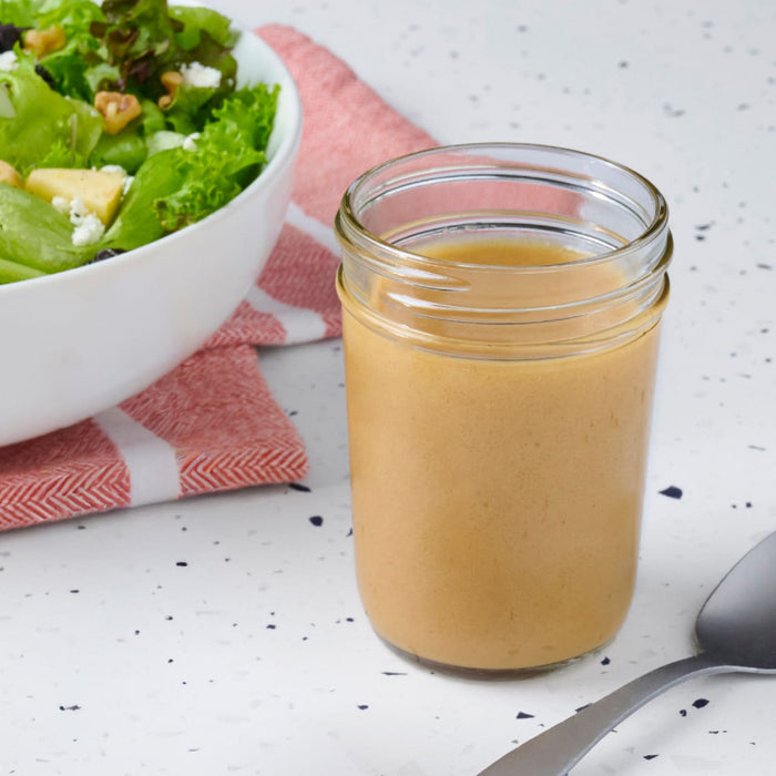 A jar of homemade salad dressing sits next to a fresh salad, suggesting a healthy and delicious meal option.
