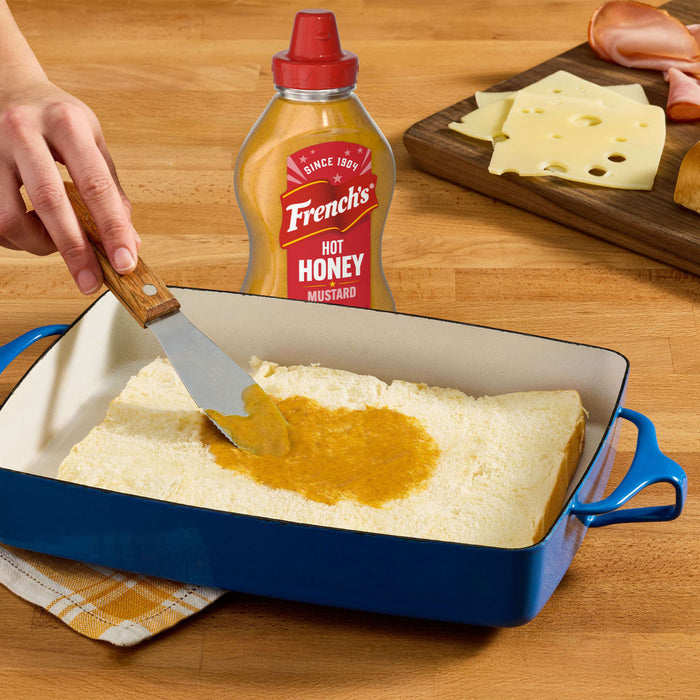 A person spreads a brown sauce over a layer of white cake in a blue baking dish.