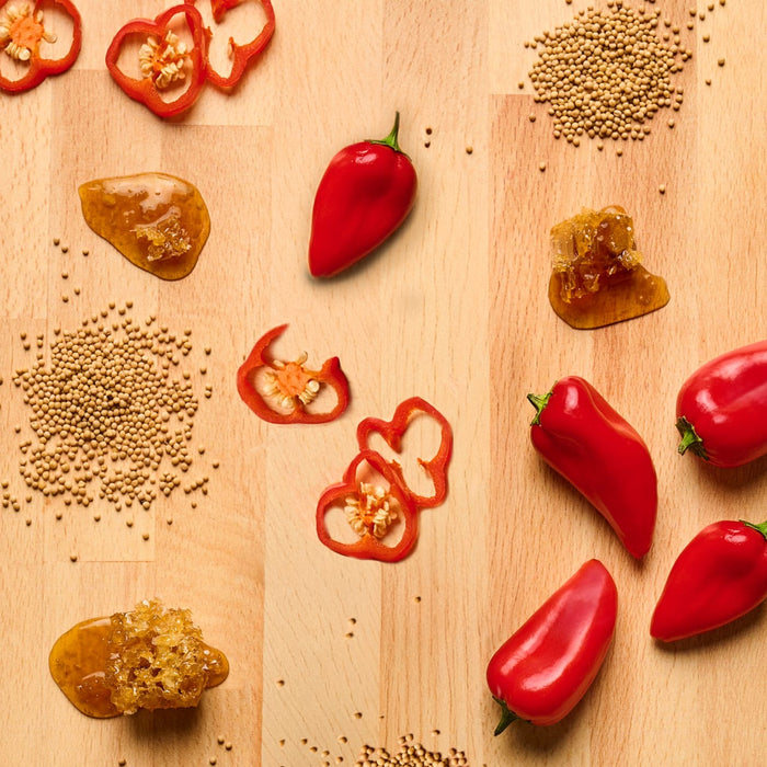 A wooden surface displays red peppers, pepper slices, seeds, and a honey-like substance, suggesting ingredients for a spicy and sweet culinary creation.