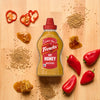 A wooden surface displays red peppers, pepper slices, seeds, and a honey-like substance, suggesting ingredients for a spicy and sweet culinary creation.