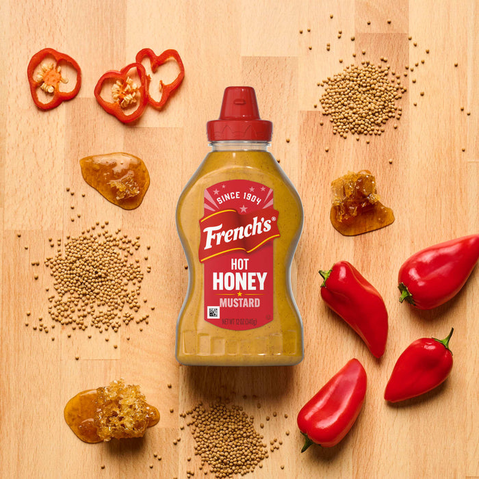 A wooden surface displays red peppers, pepper slices, seeds, and a honey-like substance, suggesting ingredients for a spicy and sweet culinary creation.
