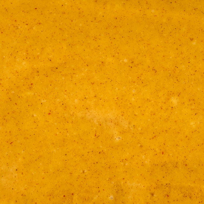 A close-up texture of a vibrant orange-yellow sauce with visible spice particles.