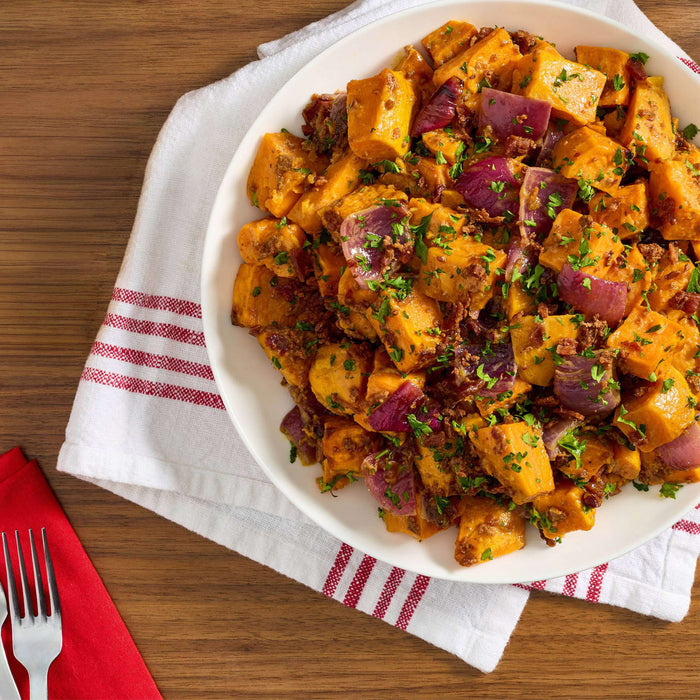 A plate of roasted sweet potatoes and red onions, garnished with herbs, sits on a red and white striped napkin.