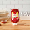 A bottle of French S Tomato Ketchup, 20 Oz stands upside down on a wooden counter next to takeout containers and small sauce cups.