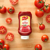 A bottle of FrenchS Tomato Ketchup, 20 Oz is centered on a wooden surface surrounded by fresh whole and sliced red tomatoes.