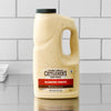 A large, half-gallon jug of Cattlemen'S Alabama White Bbq Sauce, 0.5 Gal sits on a stainless steel countertop, ready for use in a professional kitchen.