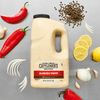 A large jug of Cattlemen'S Alabama White Bbq Sauce, 0.5 Gal is displayed on a metal surface, surrounded by fresh ingredients like red peppers, garlic, lemon, and peppercorns.